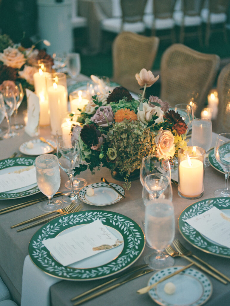 Wedding reception at the Belmond El Encanto hotel by the Lily Pond. Drapery hanging around the courtyard. White pillars with White urns full of white, pink, sand, and burgundy colored flowers. Candles lining the lily pond bridge. Green chargers, velvet linens and gold flatware. Candlelit reception.