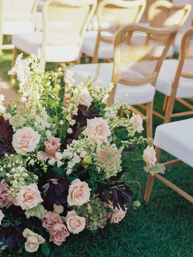 Wedding ceremony at the Belmond El Encanto hotel by the Lily Pond. Drapery hanging around the courtyard. White pillars with White urns full of white, pink, sand, and burgundy colored flowers.