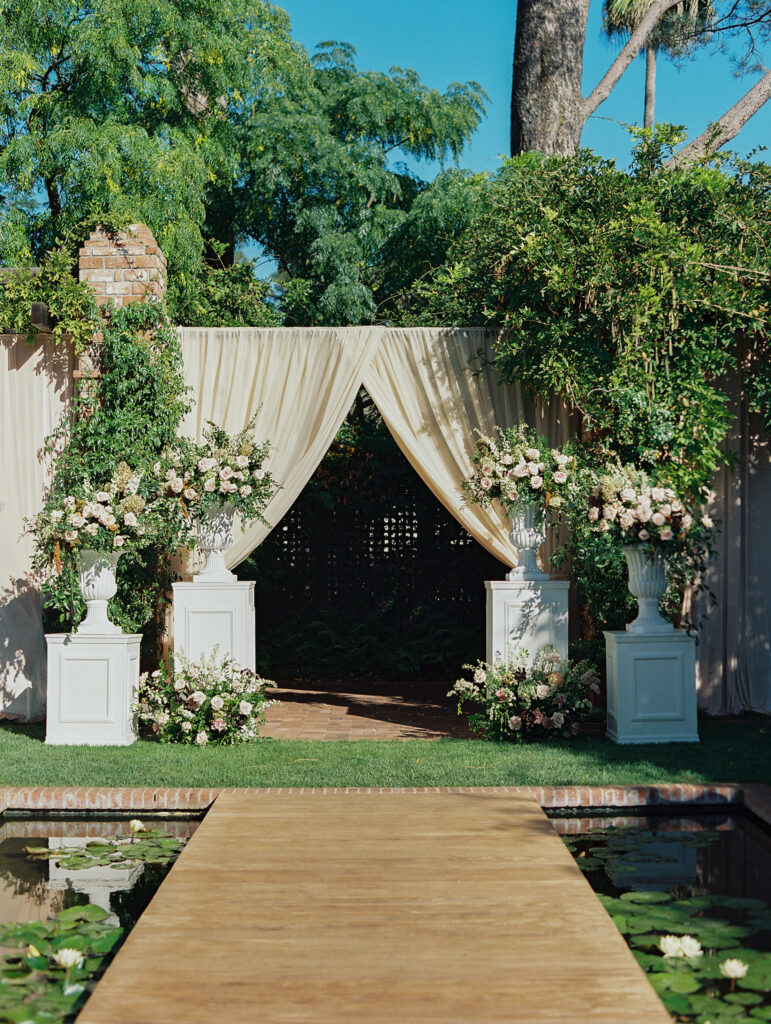 Wedding ceremony at Belmond El Encanto with Floral urn arrangements on pillars at the Lily Pond and velvet draping