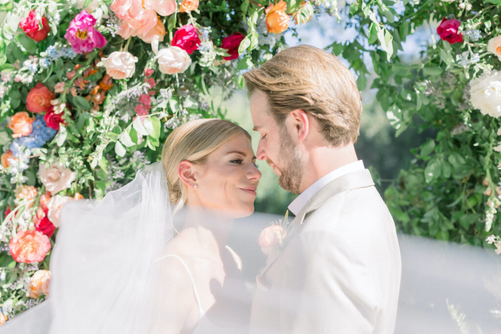 Home backyard garden wedding ceremony in Montecito with rainbow colored flowers on floral aisle, urns, and classic arch. Bride and Groom portrait.