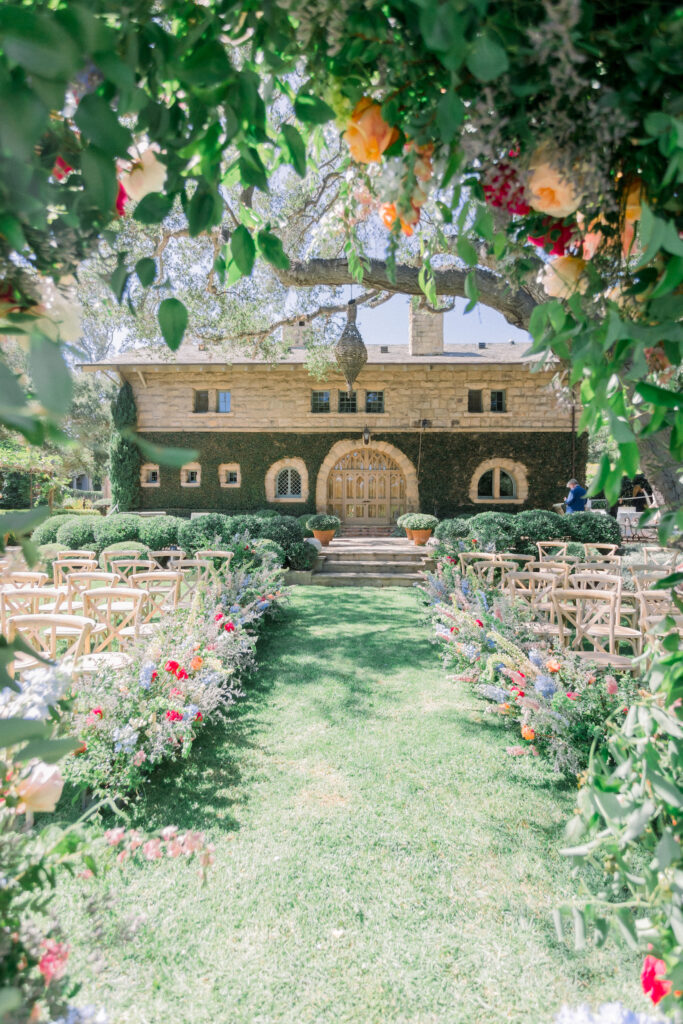 Home backyard garden wedding ceremony in Montecito with rainbow colored flowers on floral aisle, urns, and classic arch.