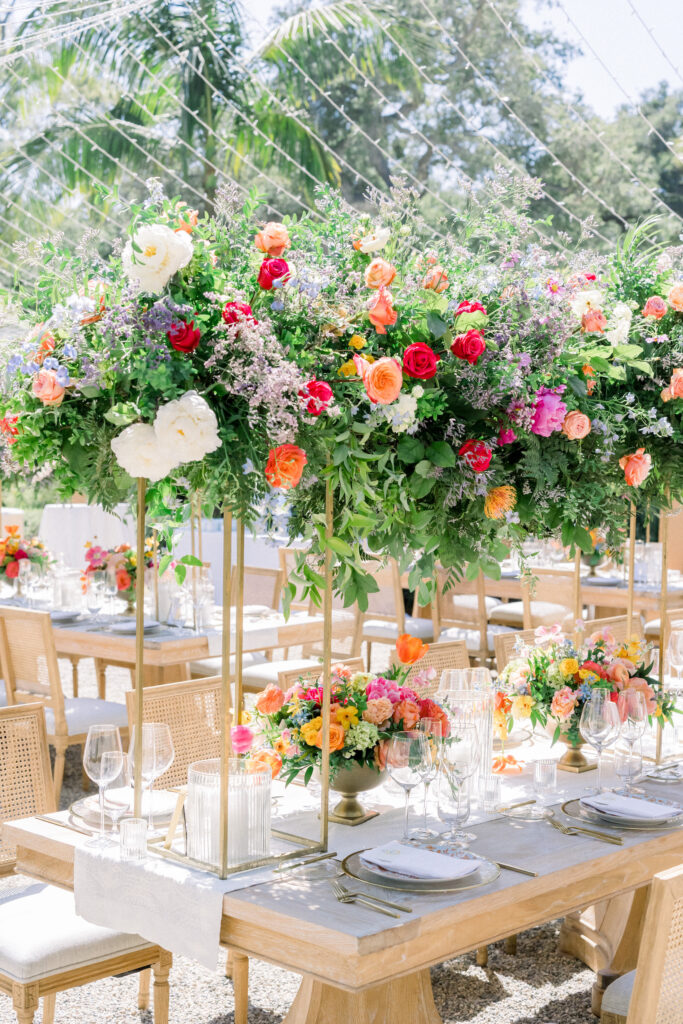 Montecito home Backyard wedding reception with lots of Colorful flowers and light wood furniture under a canopy of fairy lights