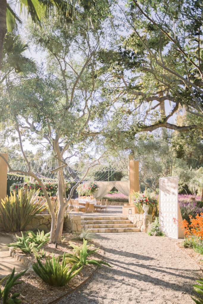 Montecito home backyard wedding reception with escort card display wall, light wood structures holding canopy of fairy lights over the dinner space.