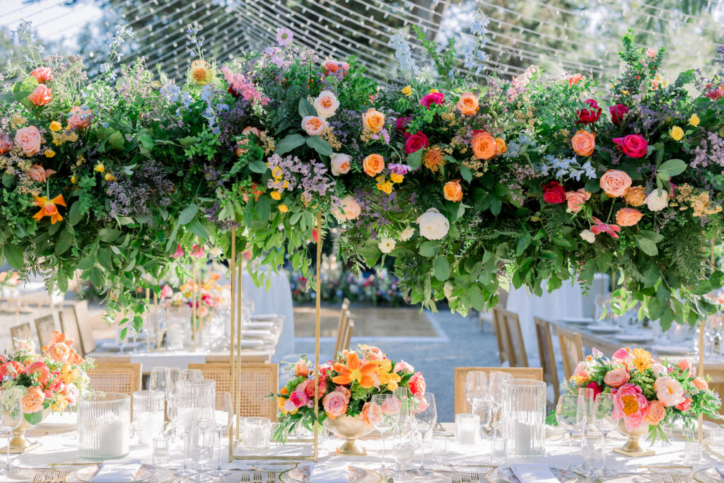 Montecito home Backyard wedding reception with lots of Colorful flowers and light wood furniture under a canopy of fairy lights