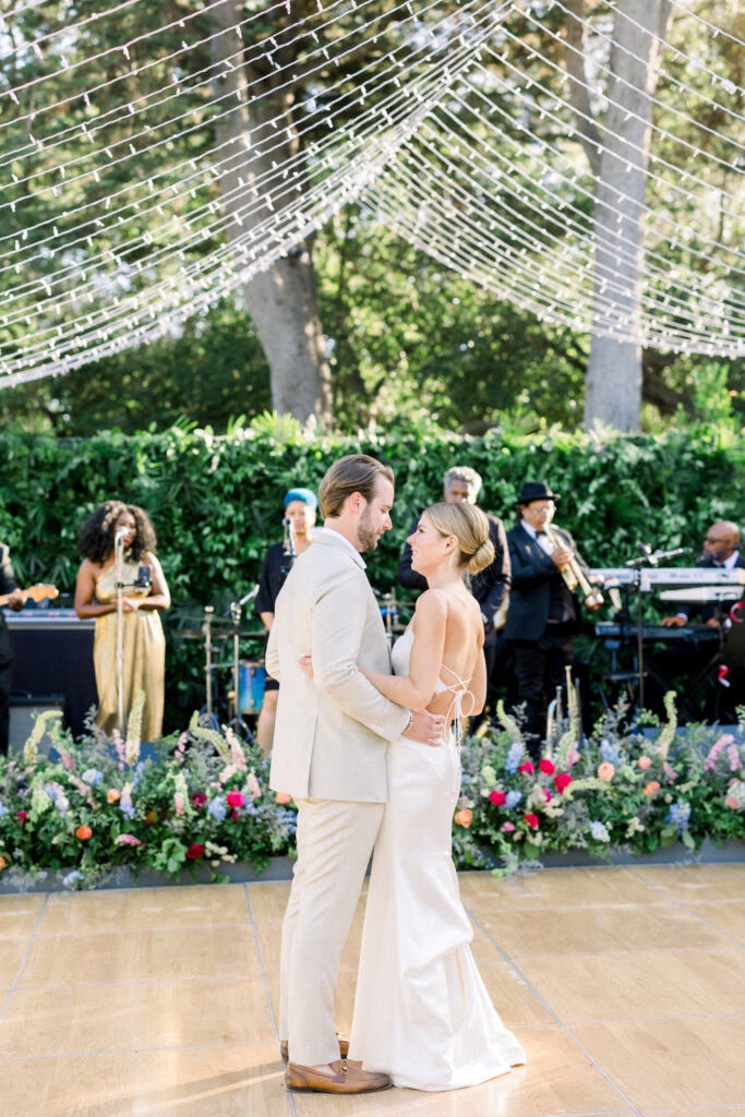 Bride and Groom first dance at their Montecito home Backyard wedding reception with lots of Colorful flowers, full band and under a canopy of fairy lights