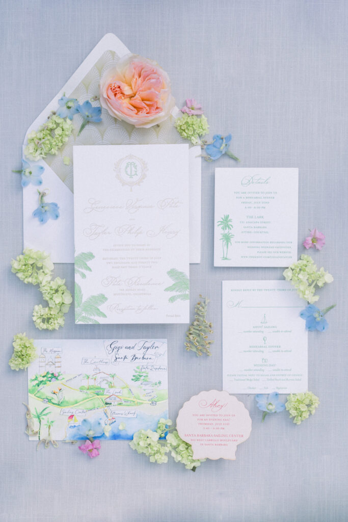 Flatlay of wedding invitation suite with flowers and watercolored map of Santa Barbara