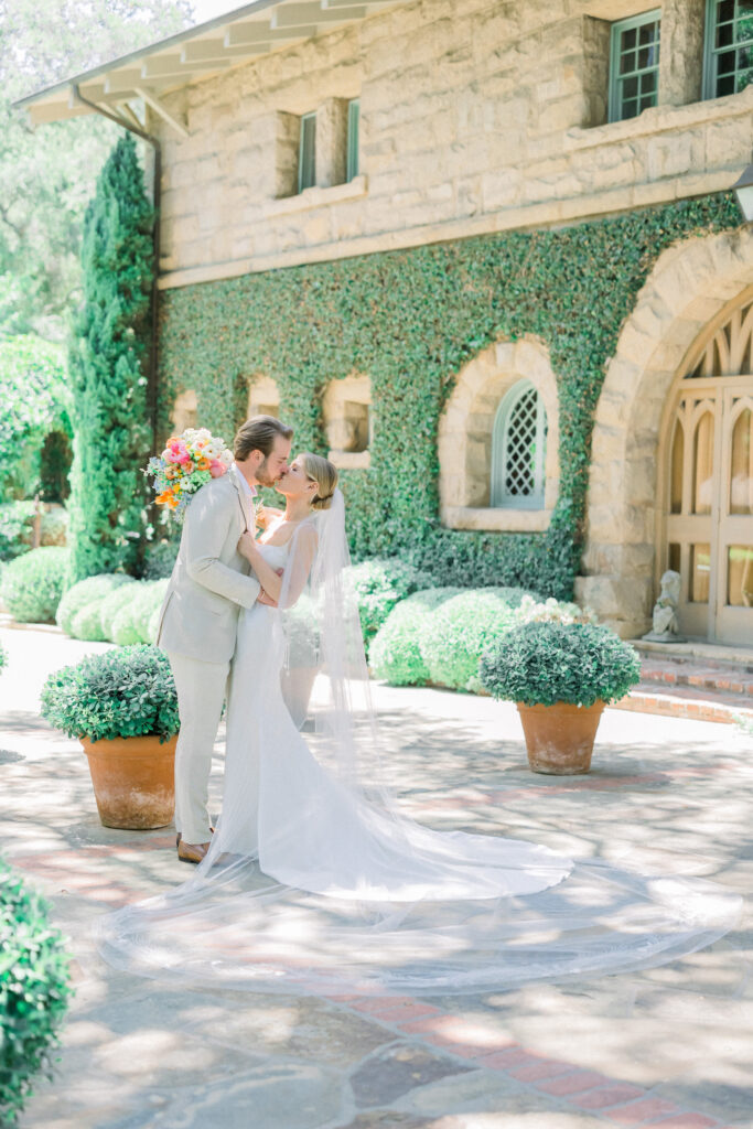 Home backyard garden wedding ceremony in Montecito with rainbow colored bouquet flowers, long veil. Bride and Groom kissing portrait.