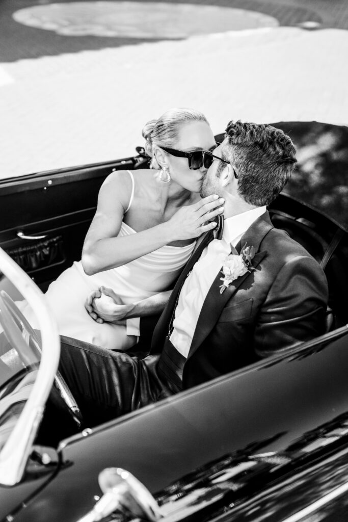 Black and white photo of bride and groom kissing in vintage car. Image by Jodee Debes