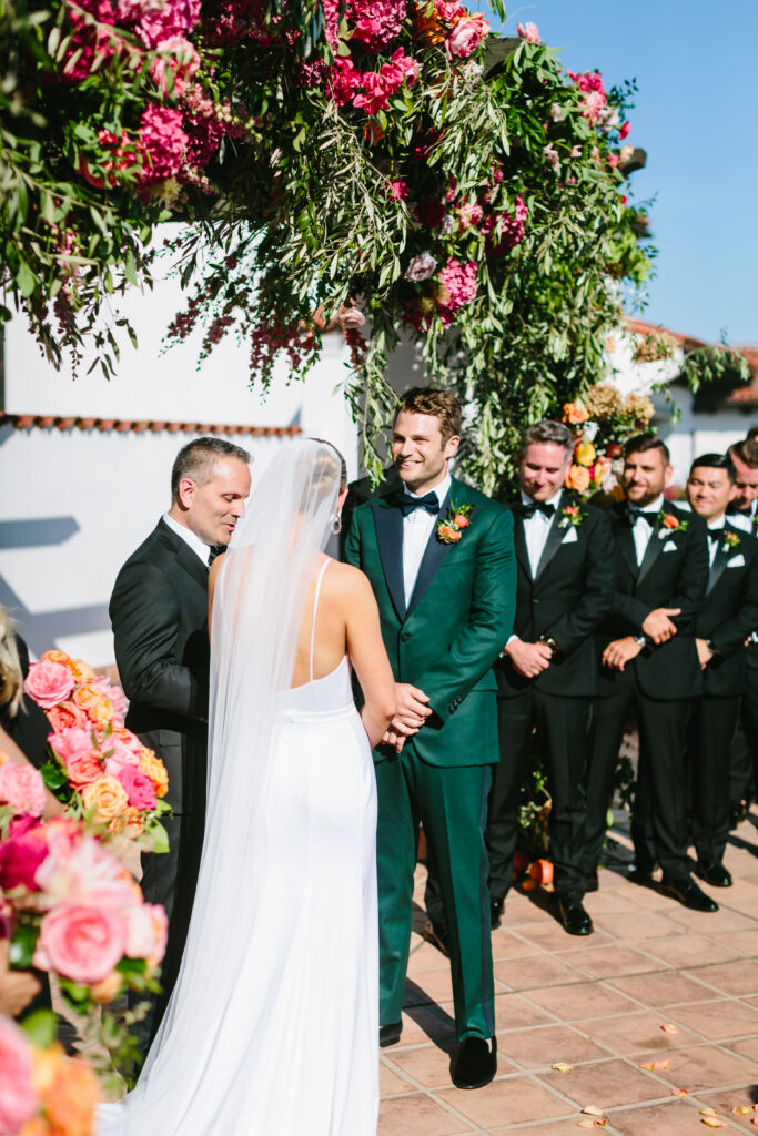 Wedding ceremony on Hotel Californian rooftop with large pink and orange floral arch. Wedding photography by Jodee Debes