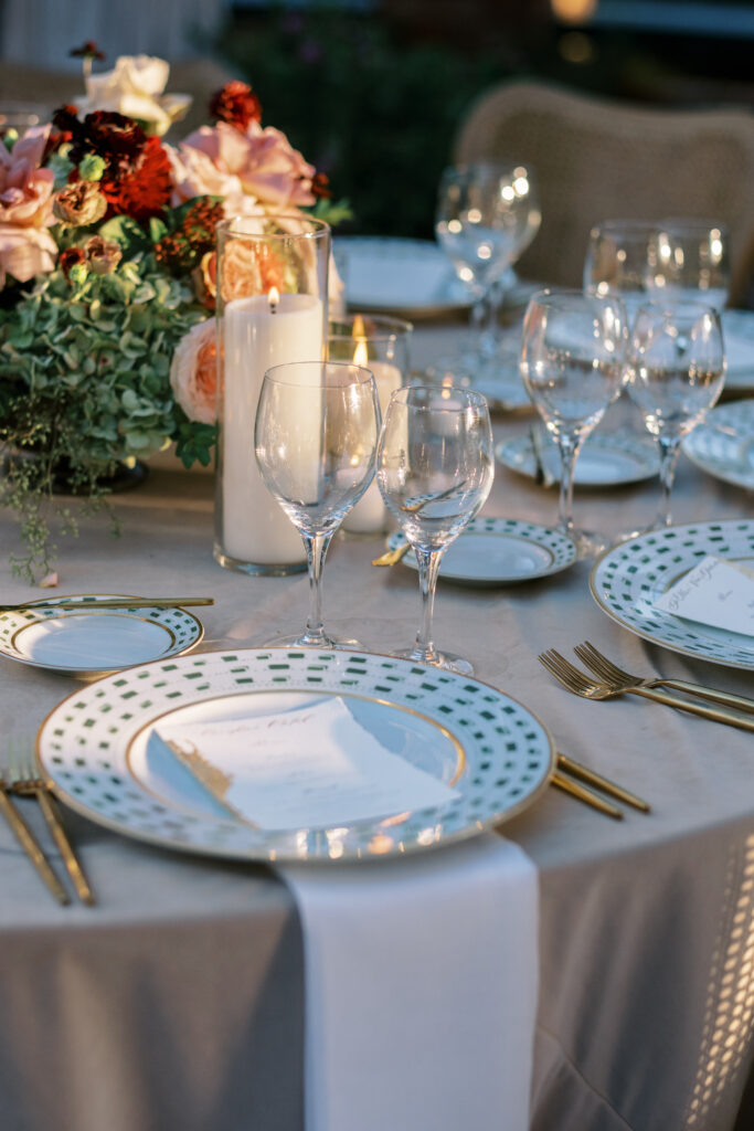 Wedding reception at the Belmond El Encanto hotel by the Lily Pond. Drapery hanging around the courtyard. White pillars with White urns full of white, pink, sand, and burgundy colored flowers. Candles lining the lily pond bridge. Green chargers, velvet linens and gold flatware.