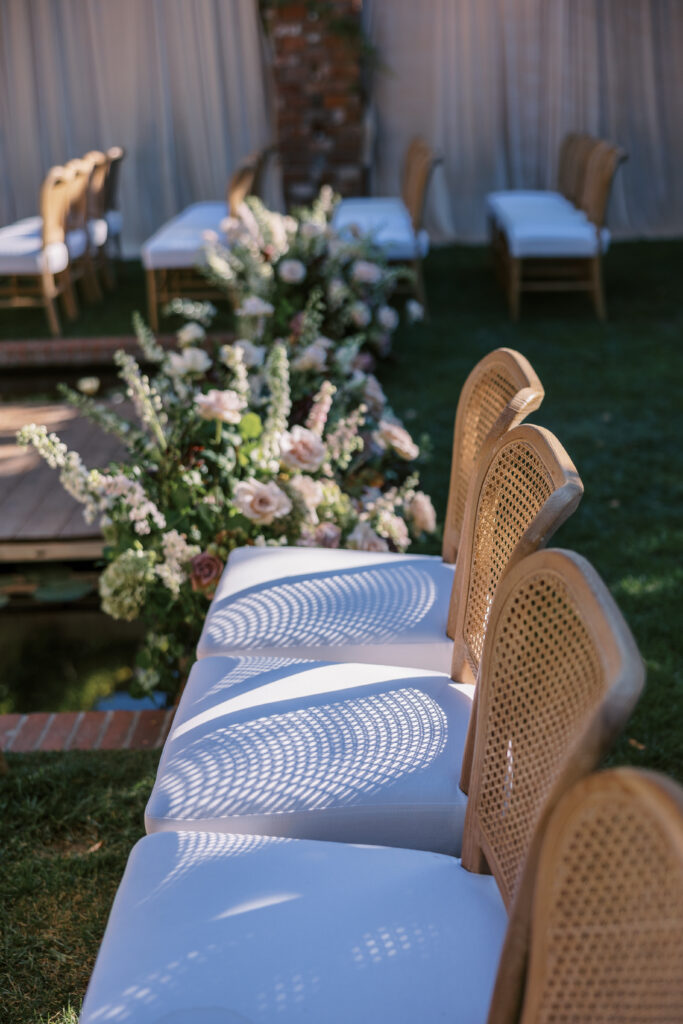 Wedding ceremony at the Belmond El Encanto hotel by the Lily Pond. Drapery hanging around the courtyard. White pillars with White urns full of white, pink, sand, and burgundy colored flowers.