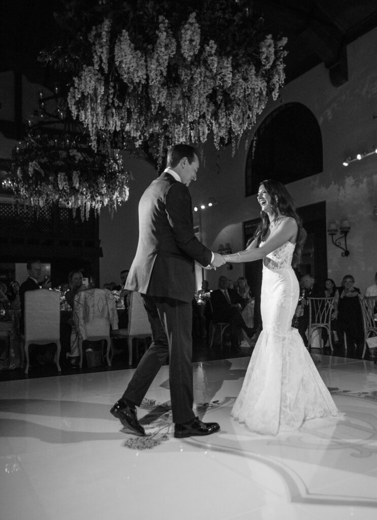 Black and white photo of Whimsical wedding reception inside the Montecito Country Club. Wisteria hanging down from chandeliers, custom dance floor 