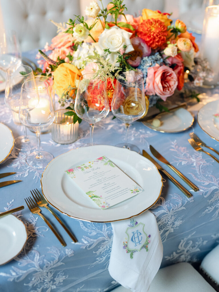 Colorful and Whimsical wedding reception inside the Montecito Country Club. Blue linens with patterned overlay, custom napkins with couple's monogram, colorful floral compote centerpieces, custom floral menu design