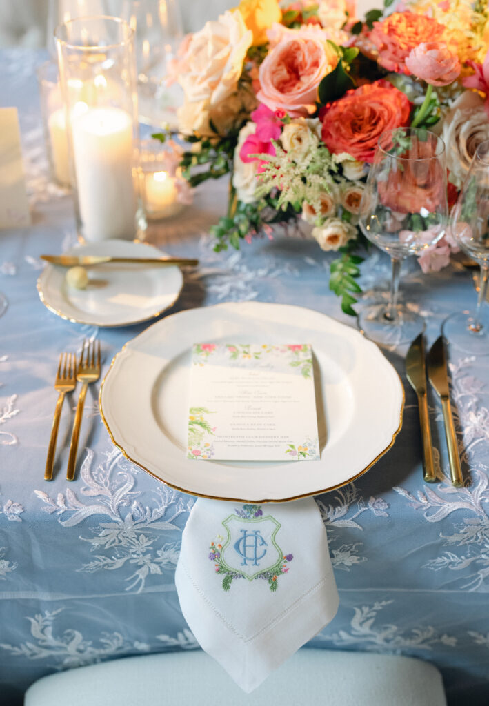 Colorful and Whimsical wedding reception inside the Montecito Country Club. Blue linens with patterned overlay, custom napkins with couple's monogram, colorful floral compote centerpieces, custom floral menu design