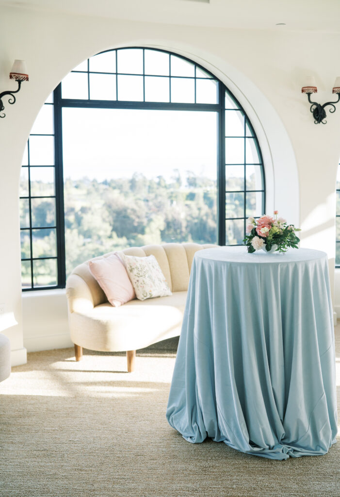 Wedding cocktail hour inside the Montecito Country Club with light blue velvet linens and small colorful floral arrangements