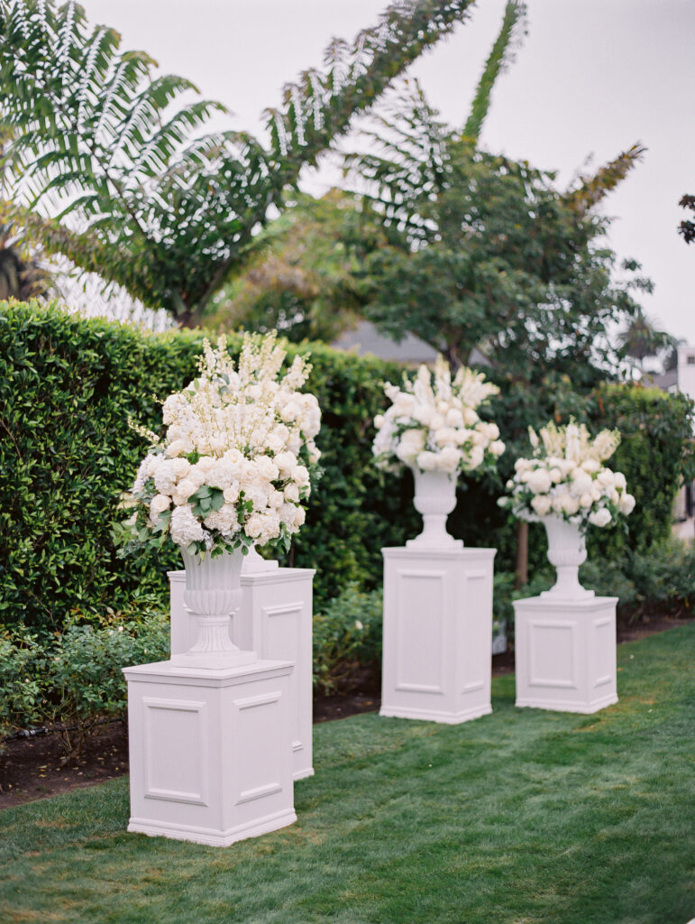 Wedding ceremony with white floral urn arrangements on top of white pillars at the Rosewood Miramar Beach resort