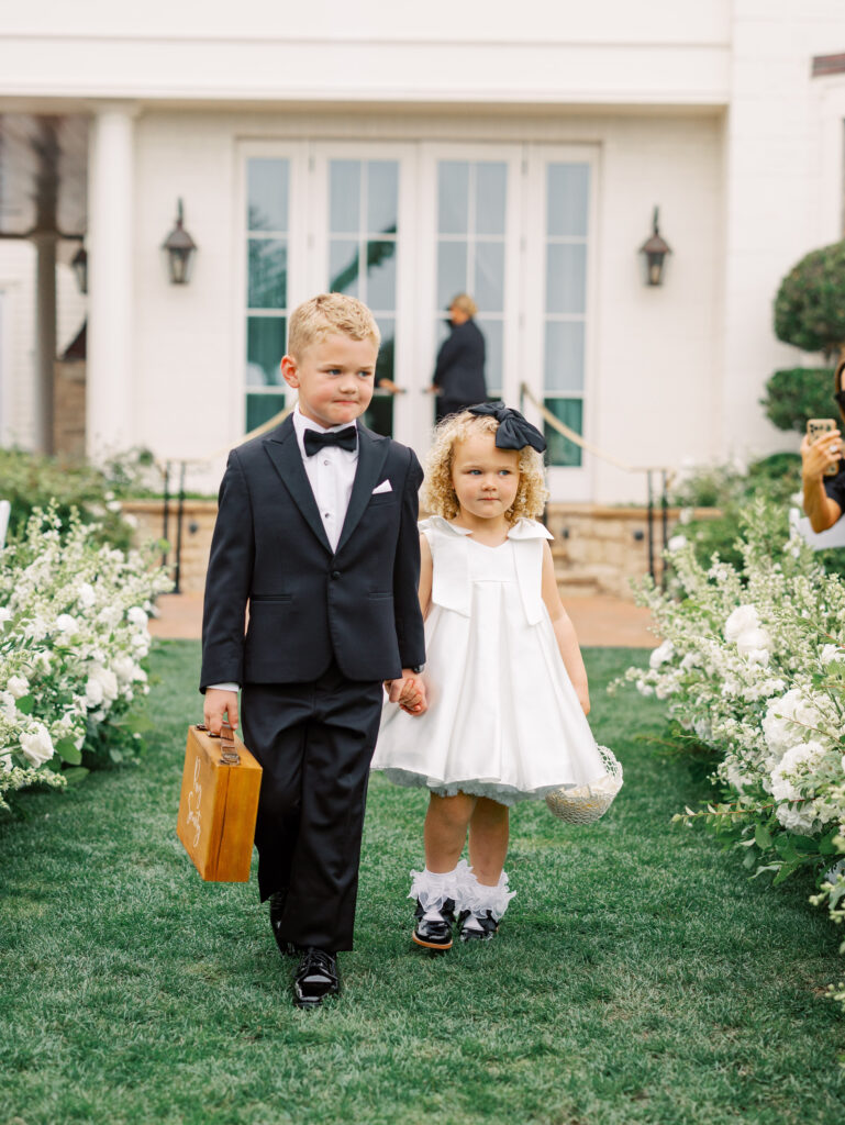 Ring bearer and flower girl walking down floral aisle at ceremony at the Rosewood Miramar Beach Resort