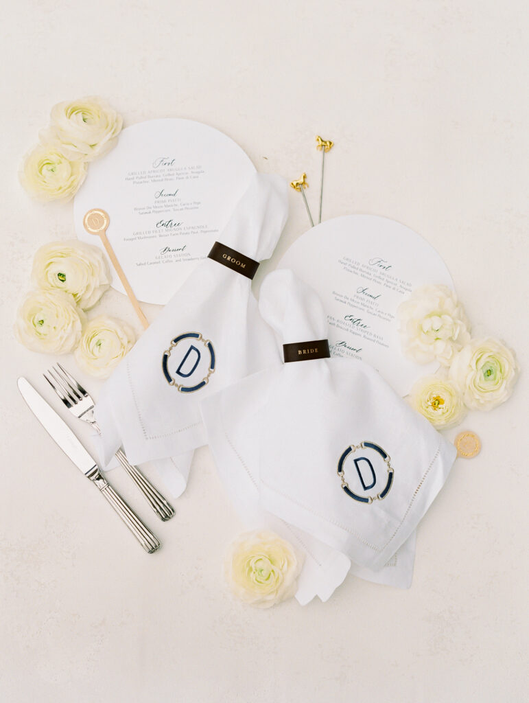 Wedding flatlay of reception details including monogramed napkins, napkin rings, stir sticks, and custom round menus