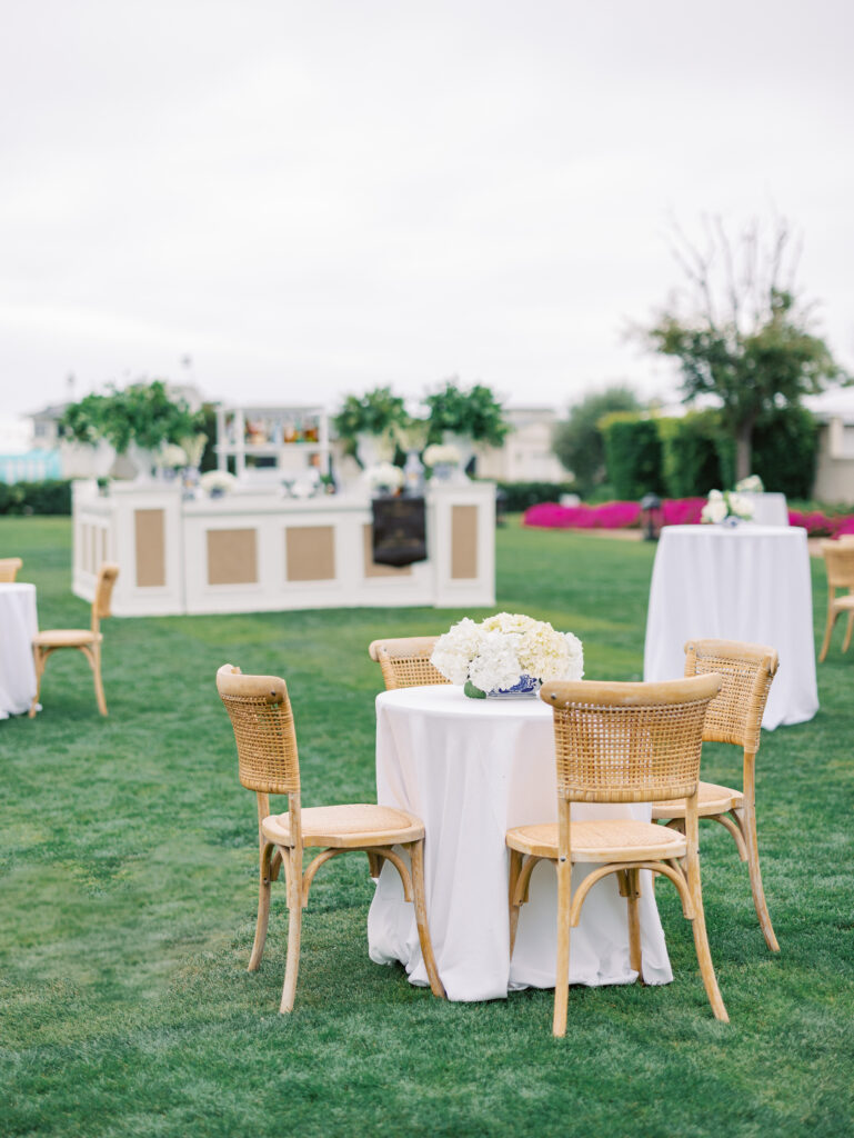 Large custom bar on the Rosewood Miramar Beach lawn at wedding cocktail hour with urns full of greenery and blue and white patterned vases