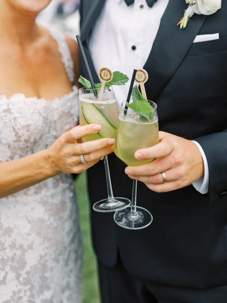 Portrait of bride and groom holding cocktails with custom stir sticks featuring their wedding monogram