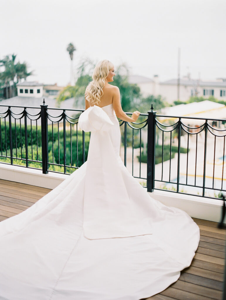 Portrait of Bride in wedding gown with big bow at Rosewood Miramar Beach Resort looking outside over fence railing