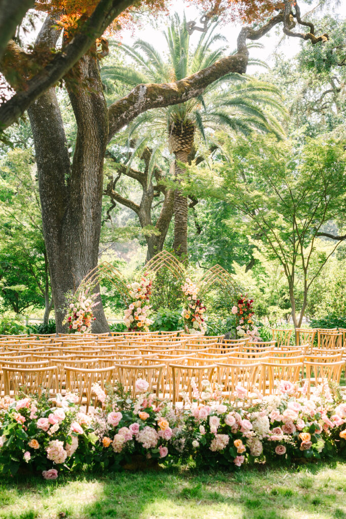 Wedding ceremony at Beaulieu Garden, Napa. Custom triple arch with burgundy and pink flowers. Back of aisle flowers.