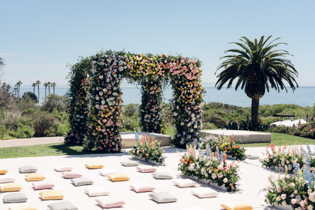 Sikh Indian Wedding at the Ritz Carlton Bacara with ocean view in background. Very large mandap and floral aisle covered in colorful rainbow flowers and carpeted ground and aisle with pillows.