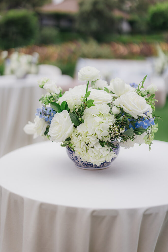 Cocktail table floral centerpiece with white and blue flowers in blue and white ginger jars on neutral linens