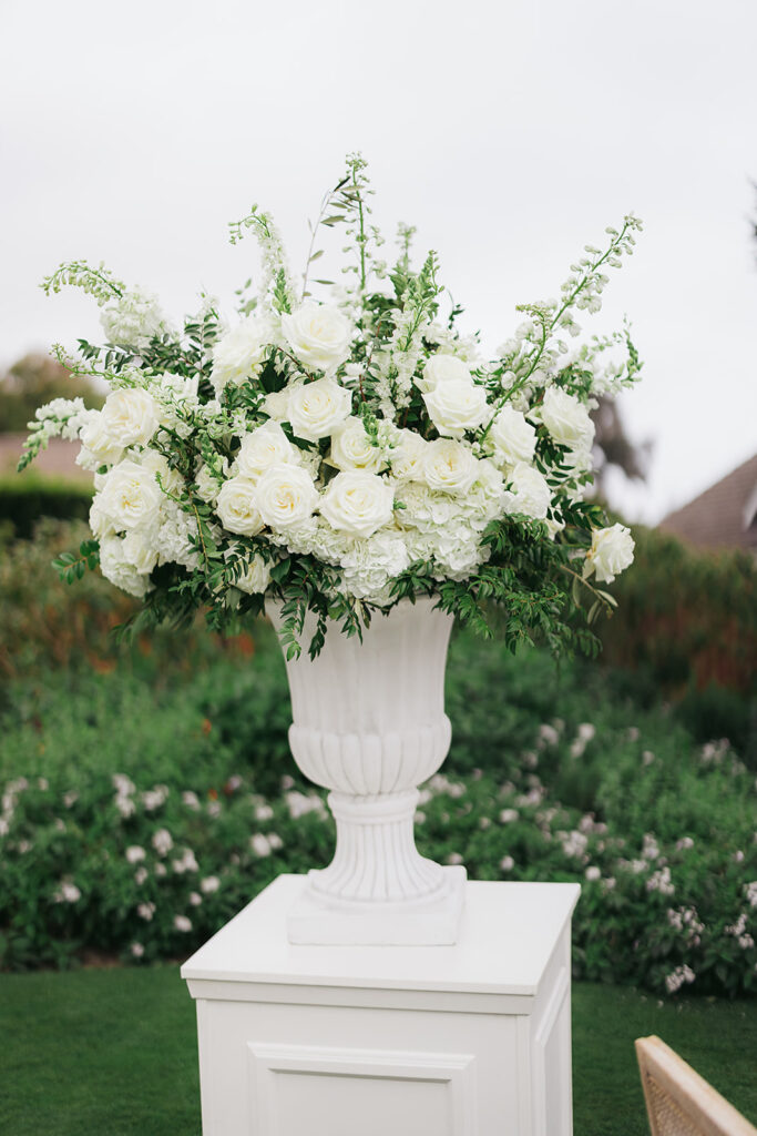 Large white urn with white floral arrangement on top of elegant white pillar