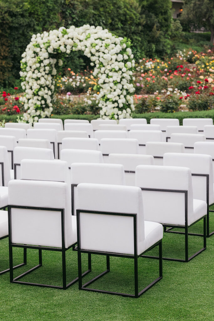 White upholstered ceremony chairs at wedding at San Ysidro Ranch in Montecito, California. Rounded wedding arch with lots of white flowers .