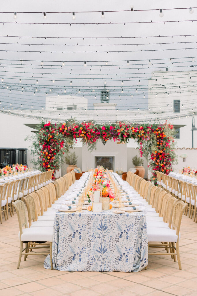 Tablescape of Wedding Welcome dinner at Hotel Californian in Santa Barbara, Ca. With colorful florals, patterned linens, and citrus details. Black string lights overhead.