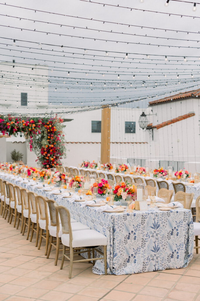 Destination Wedding Welcome Party at Hotel Californian in Santa Barbara, Ca. With colorful flowers, patterned linens, and citrus details. Tablescape with blue patterned linens and orange and pink floral centerpieces.