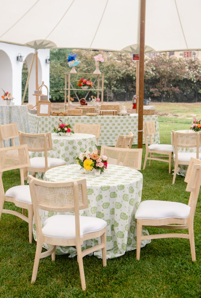 Kentucky Derby party under a white sailcloth tent with green patterned linens, cane back chairs, and colorful floral centerpieces.