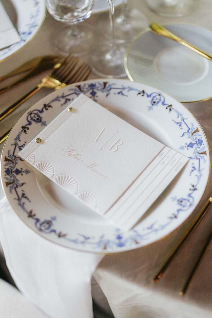 elegant white and embossed wedding menu designed in a booklet or pamphlet style laying on elegant blue patterned plate