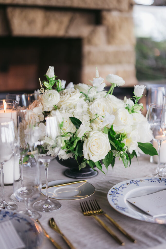 Closeup photo of white and green floral centerpieces at wedding reception dinner at San Ysidro Ranch's award-winning restaurant, Stonehouse. Neutral velvet table linens with blue elegant patterned plates.