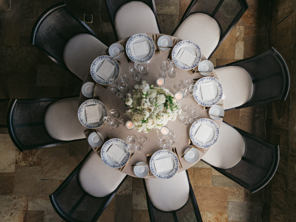 Aerial photo of wedding dinner table at San Ysidro Ranch's award-winning restaurant, Stonehouse. Neutral velvet table linens, black and white upholstered dining chairs, white and green floral centerpieces.