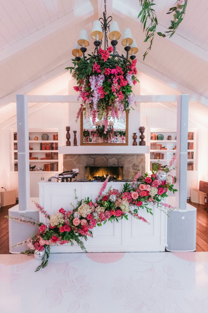 Wedding dance floor with pink floral installations on DJ booth and hanging down from chandelier. Custom white dance floor with pink floral pattern and couple's monogram